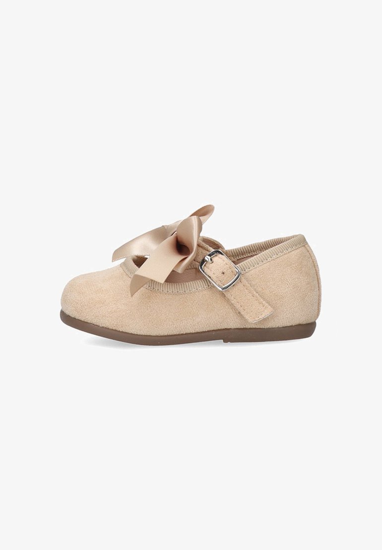 Zapato Mary Jane de gamuza beige con lazo de satén, correa con hebilla ajustable y suela plana marrón, diseñado para niños pequeños o jóvenes.