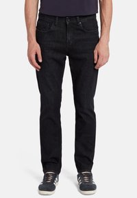 Jeans in denim nero con una vestibilità dritta, design a cinque tasche, chiusura a bottoni, leggera scoloritura e abbinati a sneakers grigie.