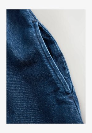 Tissu en denim bleu foncé avec une texture subtile. Légère brillance mettant en valeur les détails de couture le long du bord. Vue rapprochée d'un pli de tissu.