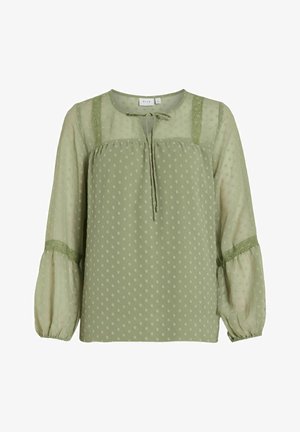 Grønn bluse med prikker og avslappet passform, med rund hals, knytedetalj og gjennomsiktige puffermed blondeaksenter på skuldrene.