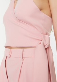 Różowy top z kopertowym dekoltem w kształcie głębokiego litery V i wiązaniem po boku. Teksturowana tkanina o gładkim wykończeniu. Połączony z wysokim stanem plisowanymi spodniami.