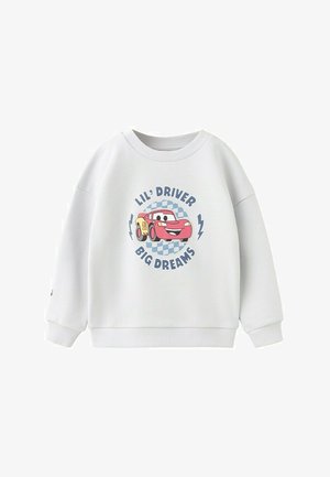 Bela otroška majica z dolgimi rokavi z risanim rdečim dirkalnim avtom in napisom »Lil' Driver Big Dreams« na sprednji strani, z modrim karo ozadjem.