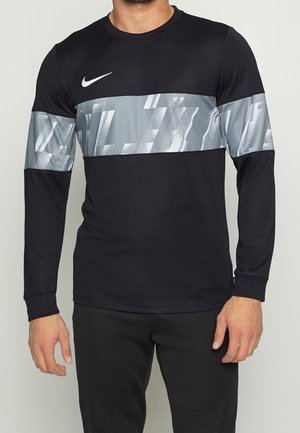 Mann trägt ein schwarzes Nike-Langarmshirt mit einem breiten grauen abstrakten Musterstreifen über Brust und oberen Ärmeln.