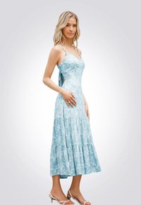 Abito maxi azzurro chiaro con motivo floreale, spalline sottili e gonna a strati. Tessuto morbido, corpino attillato e dettaglio sulla schiena aperta.