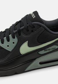 Sneaker nera con tomaia testurizzata e dettagli verdi, con marchio Gore-Tex e un design distintivo della suola intermedia con dettagli scanalati.