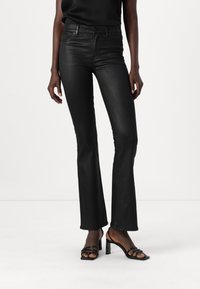 Black flared jeans made of smooth denim, featuring a high waistband, subtle stitching, and a fitted silhouette, paired with black heeled sandals.