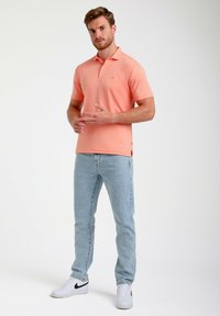 Ljusrosa polo skjorta med korta ärmar, kompletterad med ljusblå jeans och vita sneakers med svarta detaljer. Enkel design, utan mönster.