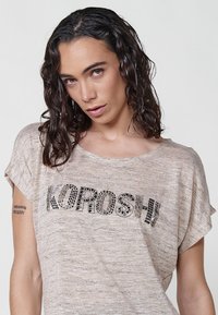 Gaiši pelēks īsām piedurknēm T-krekls ar teksturētu audumu. Uzraksts "KOROSHI" izliekts melnā krāsā. Apaļš kakla izgriezums, brīvs piegriezums.