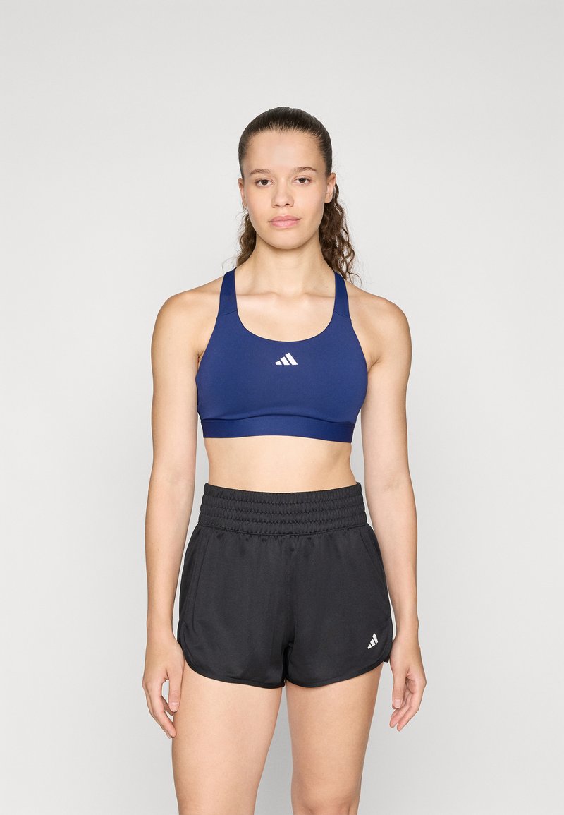 Marinblå sportbehå med rundad halsringning och vit logotyp, ihop med svarta träningsshorts med elastisk midja och sidopaneler.