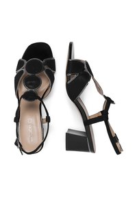 Sandalias negras de tacón con acabado de ante, con acentos circulares, diseño de punta abierta y correas en el tobillo sobre un tacón cuadrado.