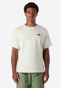 Camiseta de manga corta en tono crema, fabricada en tejido suave, con un pequeño logo negro en el pecho izquierdo. Cuello redondo y corte relajado.