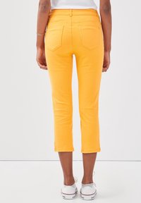 Geel cropped jeans met een gladde textuur, voorzien van een medium hoge taille, twee achterzakken en omgeslagen manchetten, gedragen met witte sneakers.
