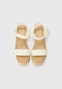 Sandales espadrilles blanches à brides avec une semelle en jute tressé, dotées d'une semelle intérieure rembourrée et de boucles de cheville ajustables pour un maintien sécurisé.