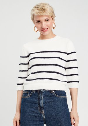 Pull rayé blanc avec des rayures horizontales navy, col rond, manches mi-longues et texture douce et duveteuse, associé à un jean en denim bleu.