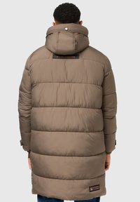 Padded rjava parka jakna s kapuco, ki ima pravokotni logotip na hrbtni strani in rebraste manšete. Gladko, trpežno blago z mat površino.