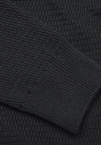 Maglia nera lavorata a maglia che mostra un motivo testurizzato con dettaglio del polsino a coste. Il materiale appare morbido e spesso.