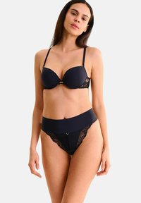 Ensemble de lingerie noire comprenant un soutien-gorge rembourré avec des accents en dentelle et un string taille haute assorti. Tissu lisse avec des bordures en dentelle détaillées.