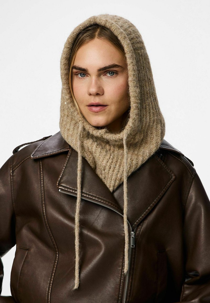 Brown leather jacket with a beige knitted hood. The hood has drawstrings and a ribbed texture. Model is facing forward with natural lighting.
