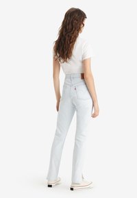 Jeans de tiro alto de color azul claro con un diseño de pierna recta, denim texturizado y un parche de cuero marrón en la parte trasera de la cinturilla.