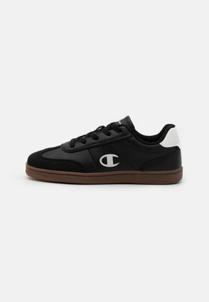 Sort lav sneakers med brun sål, hvid hælflap, sorte snørebånd og hvidt "C" logo på siden på hvid baggrund.