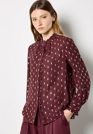 Burgundy blouse with metallic leaf pattern, button closure, ruffled neckline, and long sleeves, made from lightweight fabric.