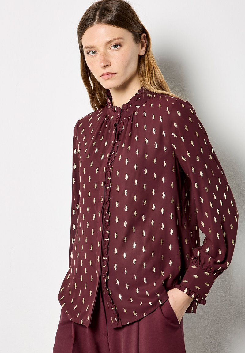 Burgundy blouse with metallic leaf pattern, button closure, ruffled neckline, and long sleeves, made from lightweight fabric.