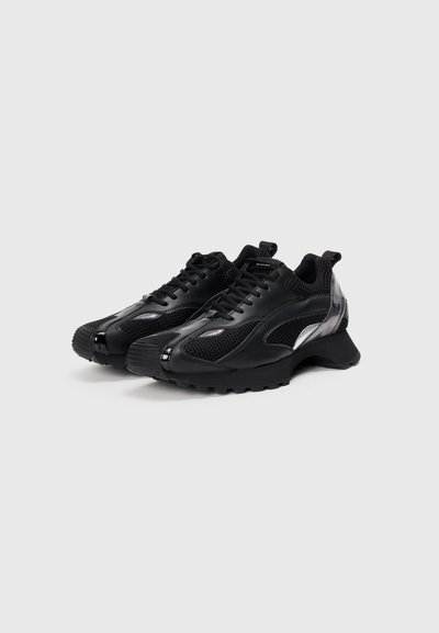 Schwarze Sneaker aus einer Mischung von Mesh- und Synthetikmaterial, mit abgerundetem Zehenbereich, dicker Gummisohle und reflektierenden Akzenten an den Seiten.
