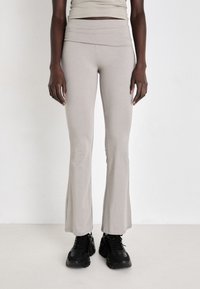 Light grey flared leggings made of soft fabric, featuring a high waistband and a smooth texture. Worn with black chunky sneakers.