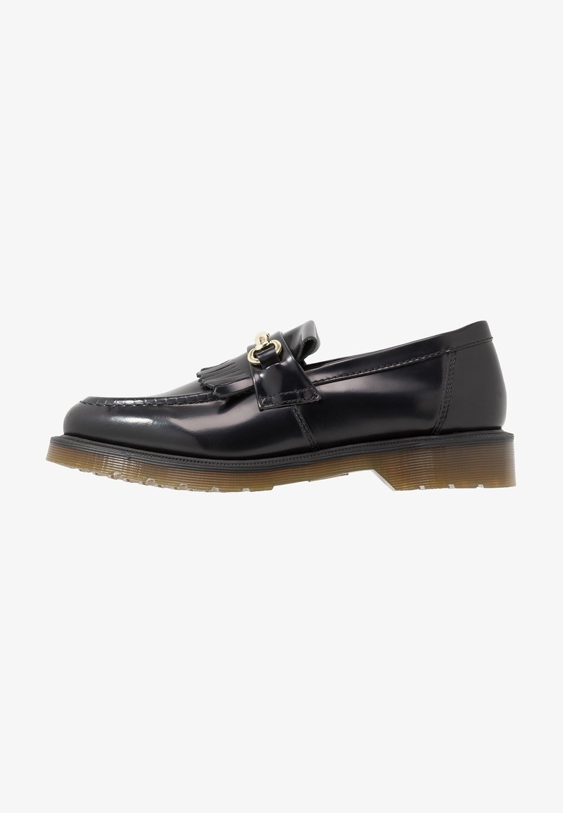 Mocassin en cuir noir avec franges et boucle dorée, semelle épaisse en caoutchouc translucide marron, et coutures style mocassin.