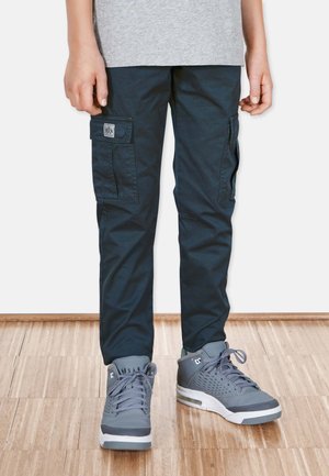 Marine cargo bukser med sidelommer, lavet af robust materiale. Båret med grå sneakers med teksturede accenter og hvide gummisåler.
