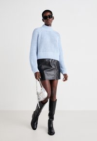 Ανοιχτό μπλε πλεκτό πουλόβερ, ψηλός γιακάς, ριγωτό μανίκι; μαύρη δερμάτινη μίνι φούστα με μπροστινό φερμουάρ; μαύρες μπότες μέχρι το γόνατο; ασημένια τσάντα.