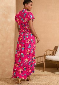 Floral maxi-jurk in felroze met geplooide mouwen, voorzien van meerkleurige bloemen en een gelaagde zoom. Draagt met tan hoge hakken.