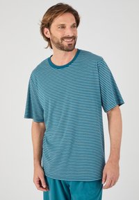 Camiseta de rayas en teal hecha de tela suave, con cuello redondo, mangas cortas y un corte relajado, combinada con pantalones teal lisos.