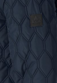 Donkerblauw doorgestikte jassectie met een zwart rechthoekig label met een driehoekig logo en de tekst "WHISTLER".