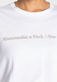 Witte katoenen T-shirt met een lichtgrijze logo met de tekst "Abercrombie & Fitch / New" aan de voorkant. Standaard ronde hals.