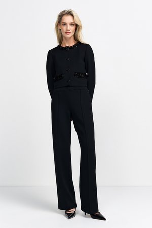 Zwarte cropped jas met glanzende kraalaccenten op de zakken, gecombineerd met zwarte op maat gemaakte broek en puntige zwarte hakken. Soepele textuur overal.