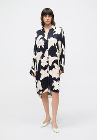 Φόρεμα πουκάμισο σε σκούρο μπλε ναυτικό με φλοράλ σχέδιο, υπερμεγέθη μακριά μανίκια, μοτίβο από άσπρα και ανοιχτό ροζ αφηρημένα φύλλα, κουμπιά μπροστά και ασύμμετρο στρίφωμα.