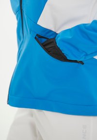 Blau-weiße Windjacke mit einem Reißverschlussfach, glattem Stoff und ergonomischem Design. Enthält schwarze Akzente am Fach.