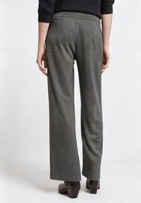 Pantalones de pierna ancha con textura gris y cintura elástica, con un patrón sutil, combinados con botines oscuros.