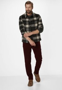 Schwarz-weiß kariertes Flanellhemd mit Knopfverschluss, über einem dunklen Hemd getragen. Kombiniert mit kastanienbraunen Hosen und hellbraunen Schuhen.