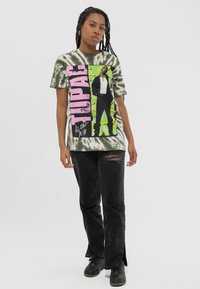 Cotton t-shirt with a tie-dye pattern in green and gray, featuring a graphic of a figure and "TUPAC" in pink, paired with black ripped jeans.