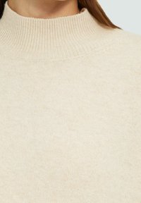 Pull à col haut beige clair avec un col côtelé, une texture tricotée et une finition douce et lisse. Design épuré sans motifs visibles.
