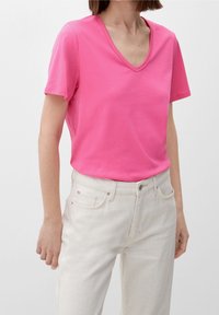 Rosa V-ringad T-shirt i bomull, kortärmad, slät textur, i kombination med ljusa denimjeans med framfickor.