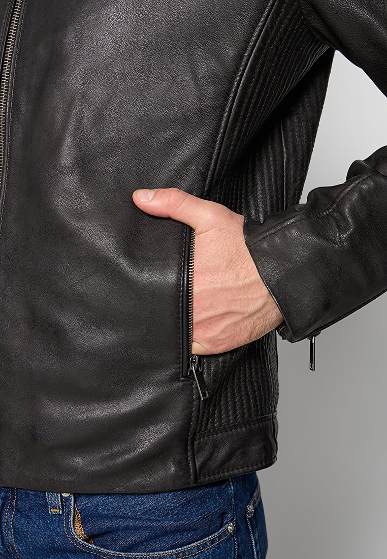 Giacca da moto in pelle nera con pannelli laterali trapuntati, tasche con zip e design aderente. Texture liscia e dettagli hardware minimalisti.