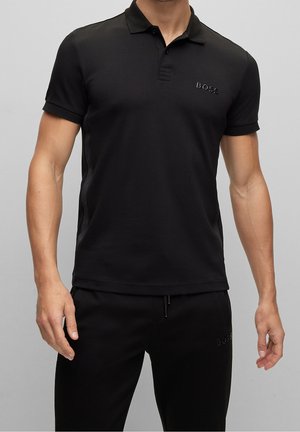 Zwarte polo met korte mouwen van gladde stof, met een drieknopenknopsluiting en mesh-details aan de zijkanten. Heeft een subtiel reliëflogo.