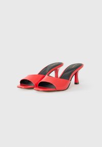 Red, patent leather heeled mules with an open toe and cross-band design. Features a slim, high heel and a cushioned black insole.
