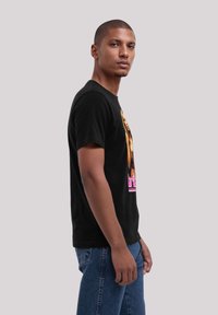 Schwarzes Baumwoll-T-Shirt mit einem Grafikdruck einer Person und fettem pinkem Text. Der Schnitt ist lässig mit kurzen Ärmeln und einem runden Halsausschnitt.