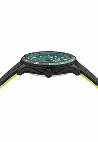 Czarny zegarek z okrągłą zieloną tarczą, żółtymi akcentami i teksturowanym gumowym paskiem. Posiada funkcję daty i wyraźną koronkę o godzinie 3.