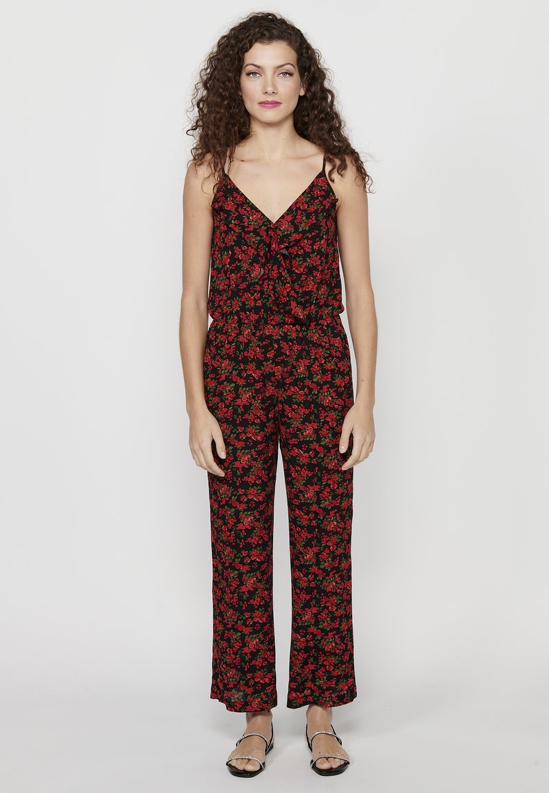 Zwarte jumpsuit met een bloemenpatroon met rode en groene accenten, dunne banden, een V-halslijn en wijde broekspijpen.