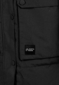 Sort stofjakke med trykknapper og en forlomme med en North Bend-logo patch i hvid.